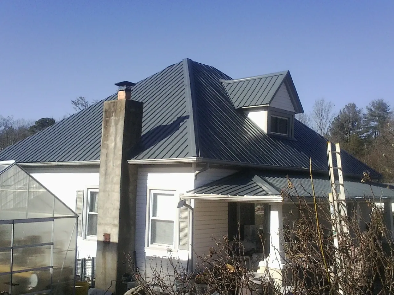 Dark blue standing seam metal roof on a white farmhouse with dormer — Slate & Tile Roof Repair by Roofing Brothers in Locust Hill