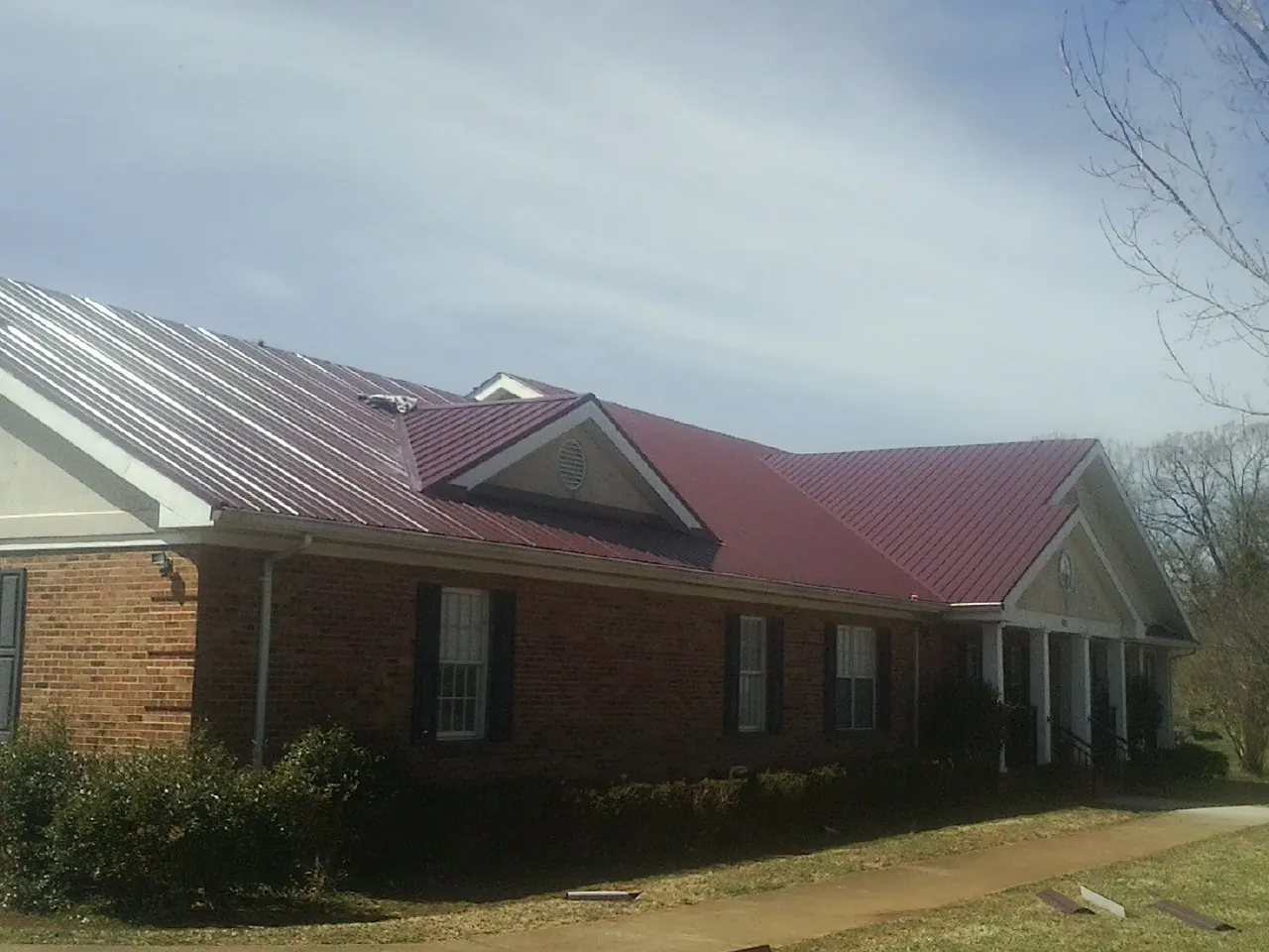 Red metal roof with gabled entries on a long brick building, from a Hail Damage Roof Repair job in Locust Hill