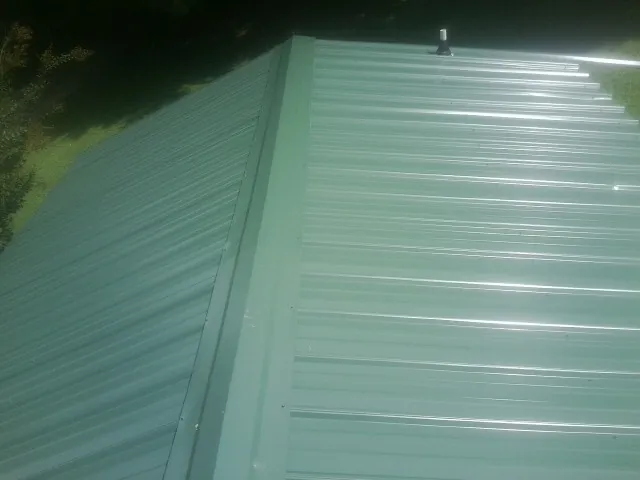 New green metal panels meeting at the ridge of a roof — Flat Roof Repair work by our crew in Locust Hill