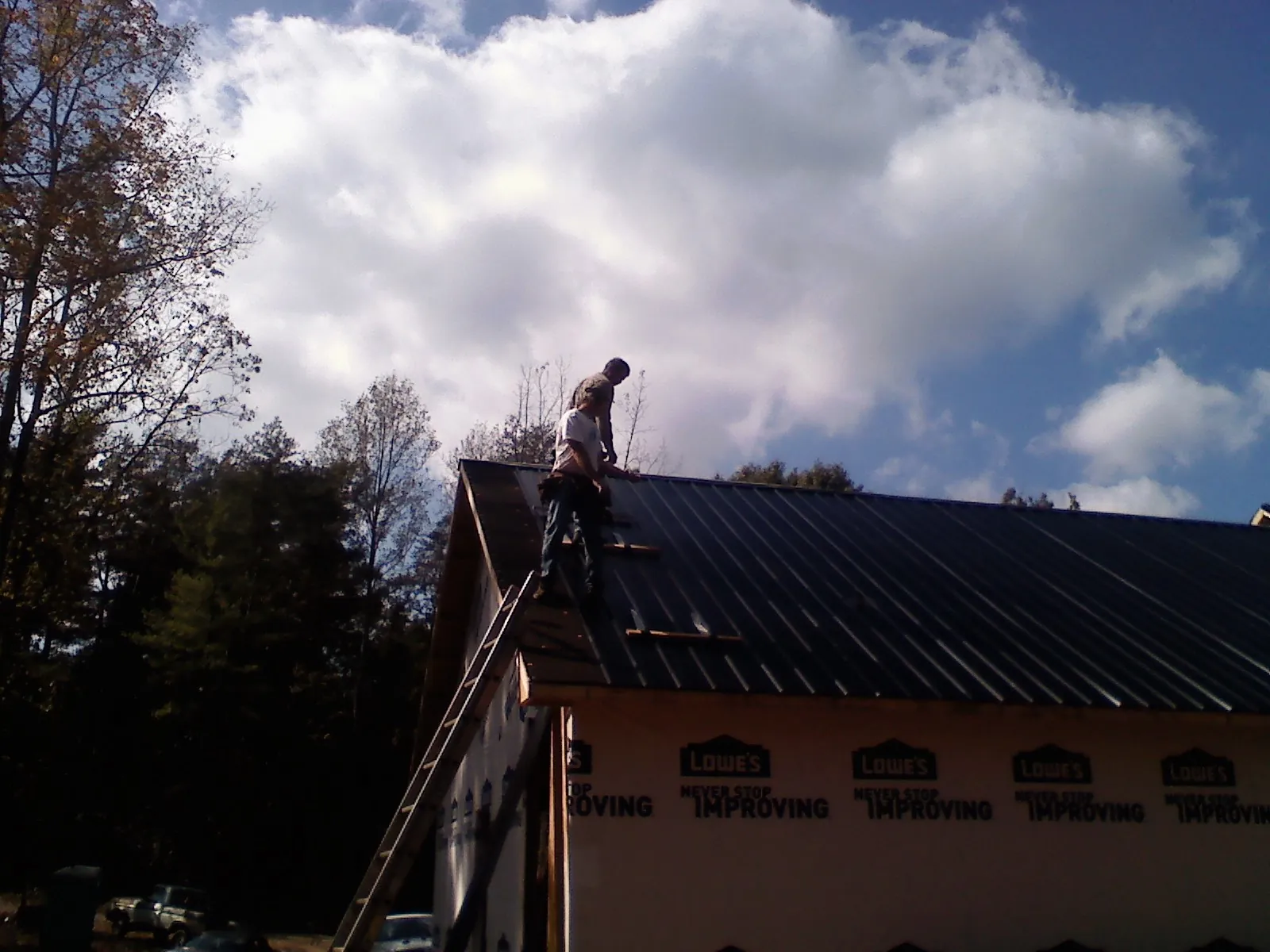 Roofer fastening dark metal panels high against a cloudy sky, from a Roof Inspection job in Locust Hill