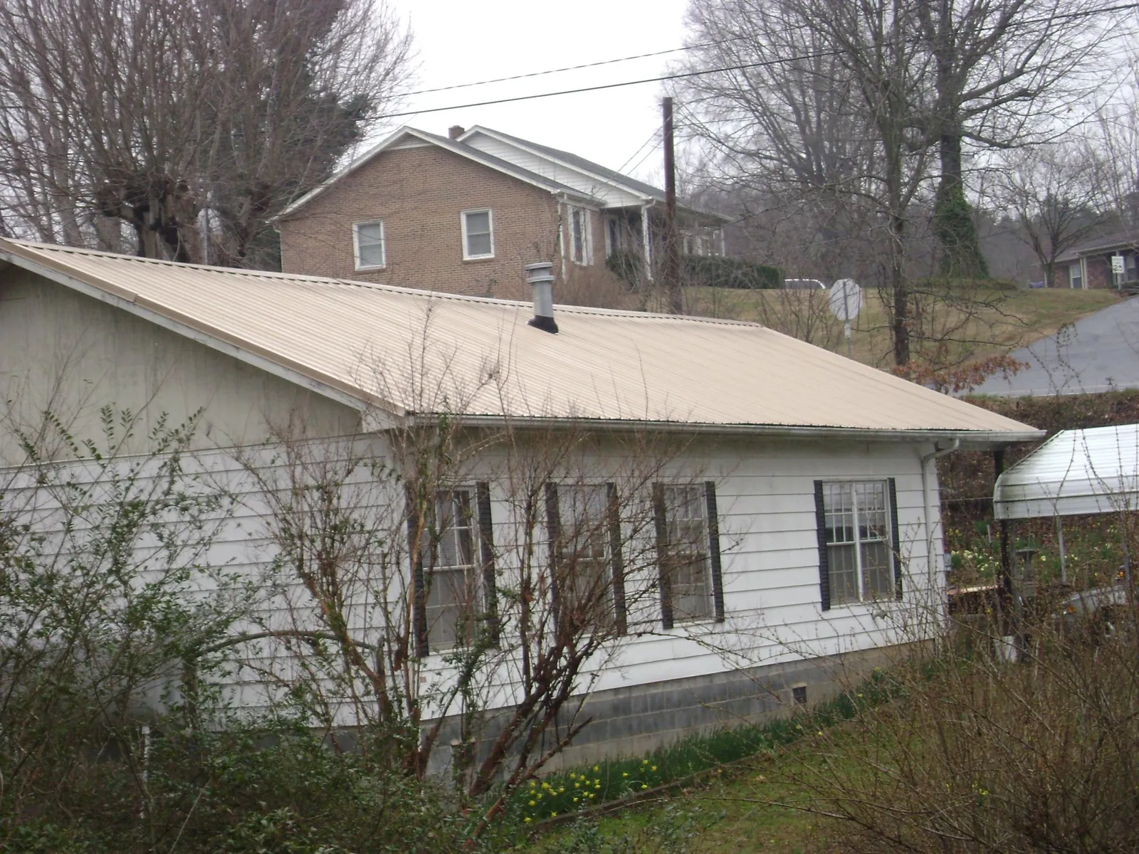 Tan metal roof on a white sided house set into a hillside — Commercial Roofing by Roofing Brothers in Locust Hill