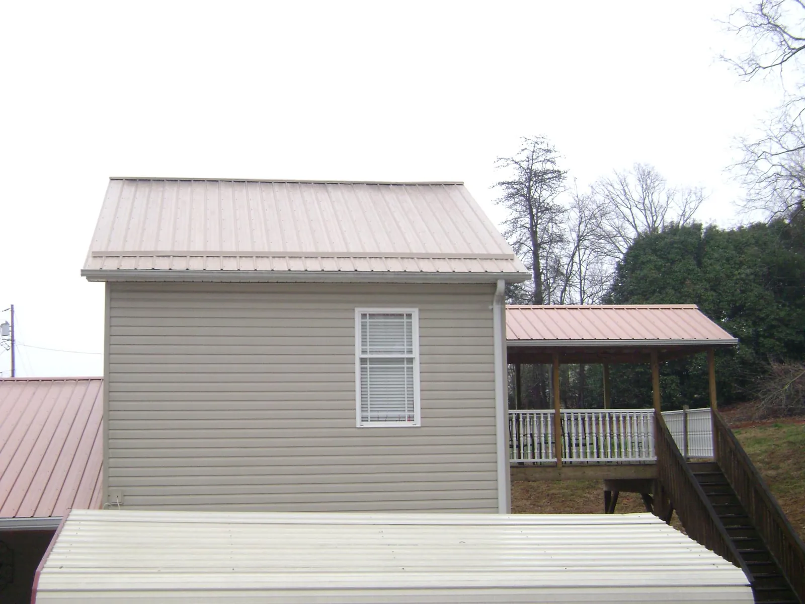 Tan metal roofs on a two story addition and attached porch, from a Roof Replacement job in Locust Hill